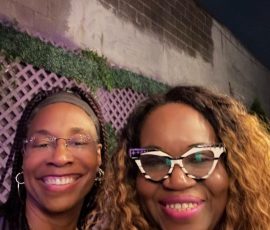 Purple is the color of connection — and these smiles say it all. Two women smiling in front of a purple-lit wall during Prince tribute gathering