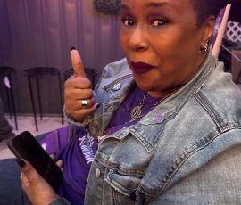 One thumb up, one purple heart — repping the Purple Rain legacy in style. Woman in denim jacket giving a thumbs-up while holding a phone during Prince celebration