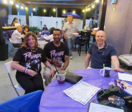Community, conversation, and a whole lot of purple. Guests seated at outdoor tables with purple tablecloths during Prince fan event