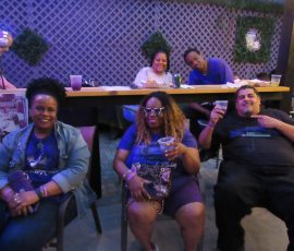 Purple pride, Long Island style — family by fandom, united by the music. Group photo of Prince fans seated in front of high bar ledge during Purple Rain anniversary party